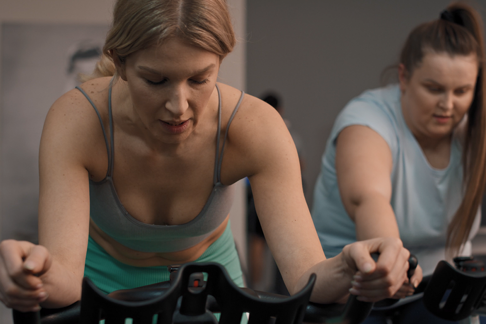 Two women exercising on stationary bikes in a gym setting.
