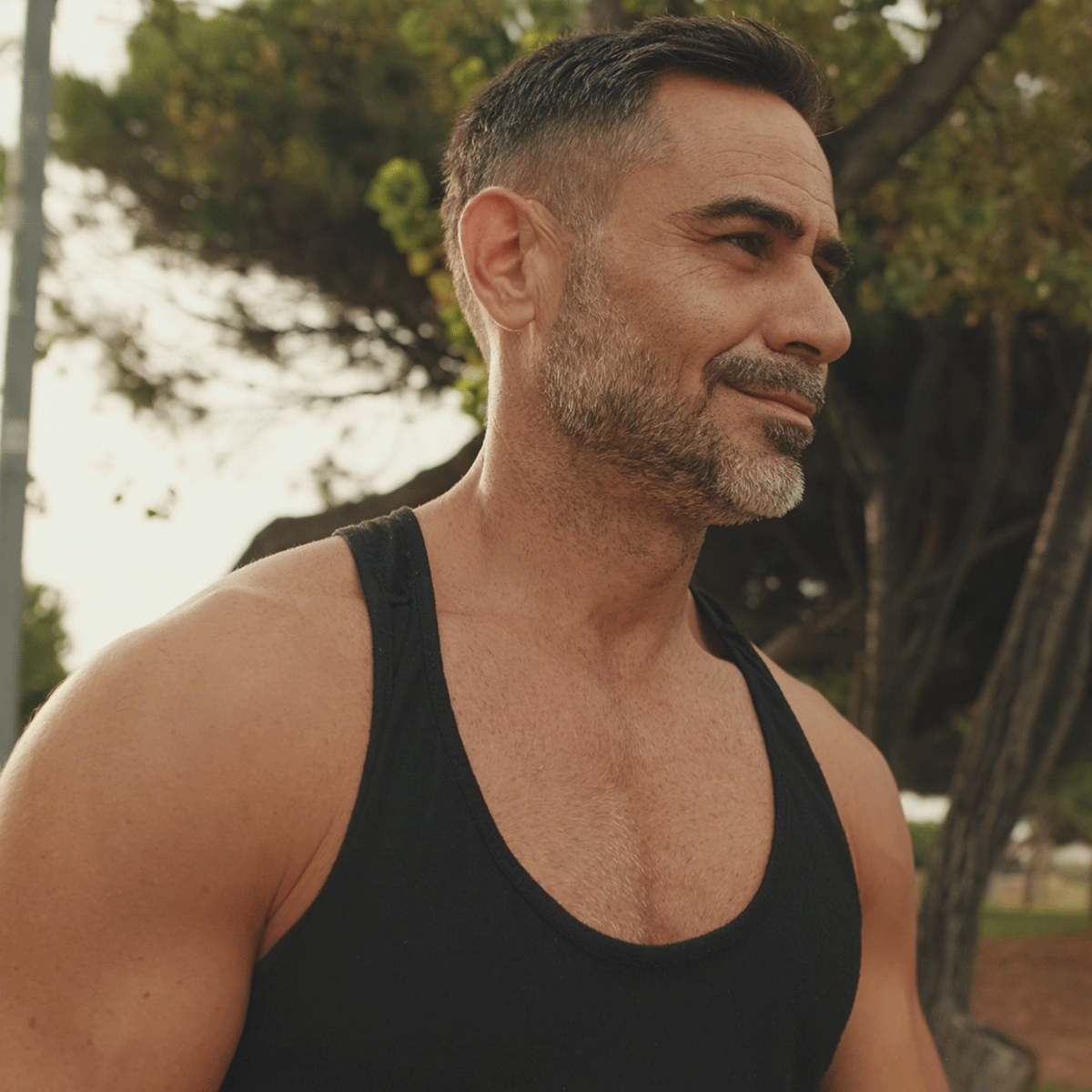 Man wearing a black tank top outdoors with trees in the background