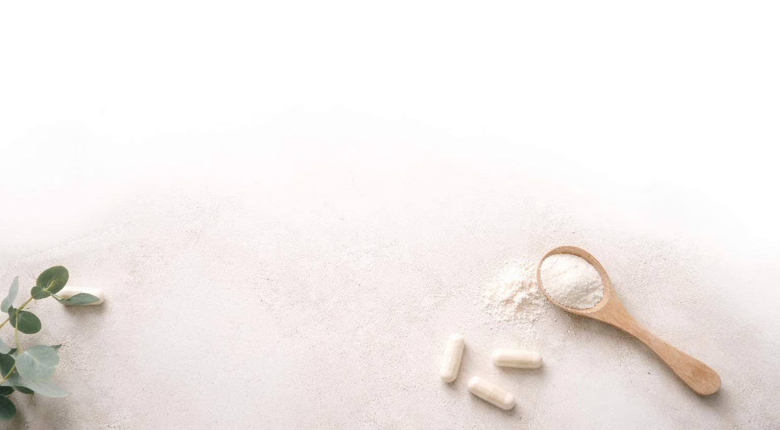 Supplements including capsules, a wooden spoon with powder, and a plant on a light background