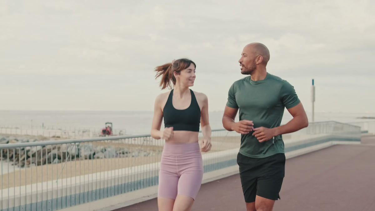A man and a woman jogging on the boardwalk near water.