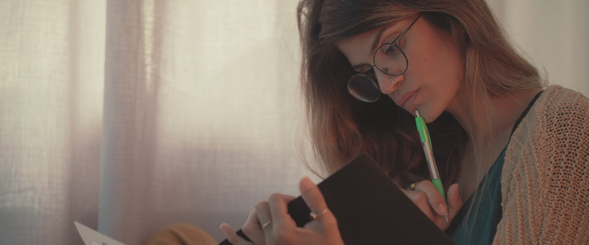 Woman looking into a notebook with pen in hand focused, concentrating, or studying.