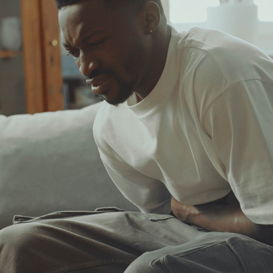 Man sitting on couch holding his stomach in discomfort.