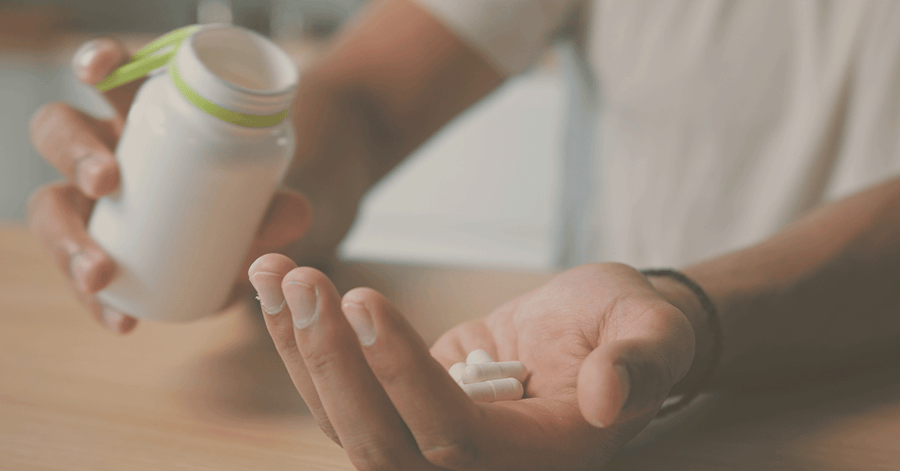 Person holding a container of supplements with pills in their hand