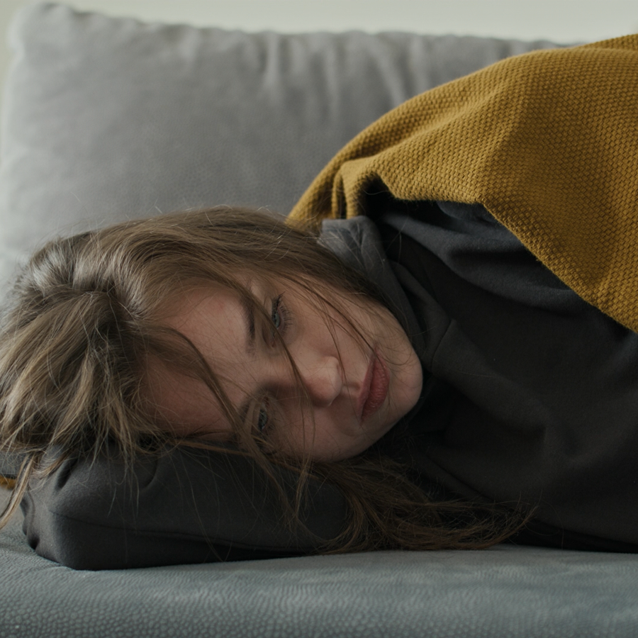 Person lying on a couch with a yellow blanket, looking sad/uncomfortable